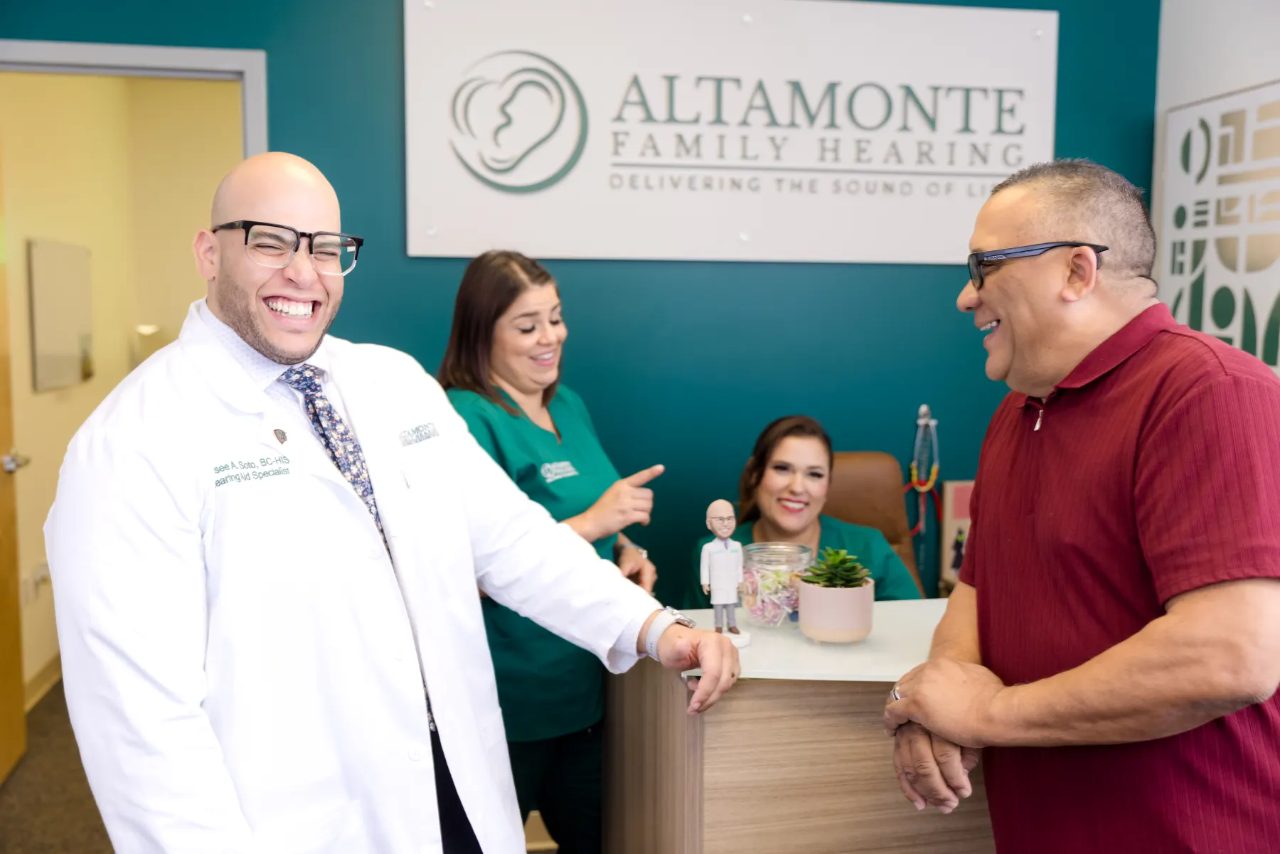 Jaysee, Grace and Francesca laughing with a patient at the front desk