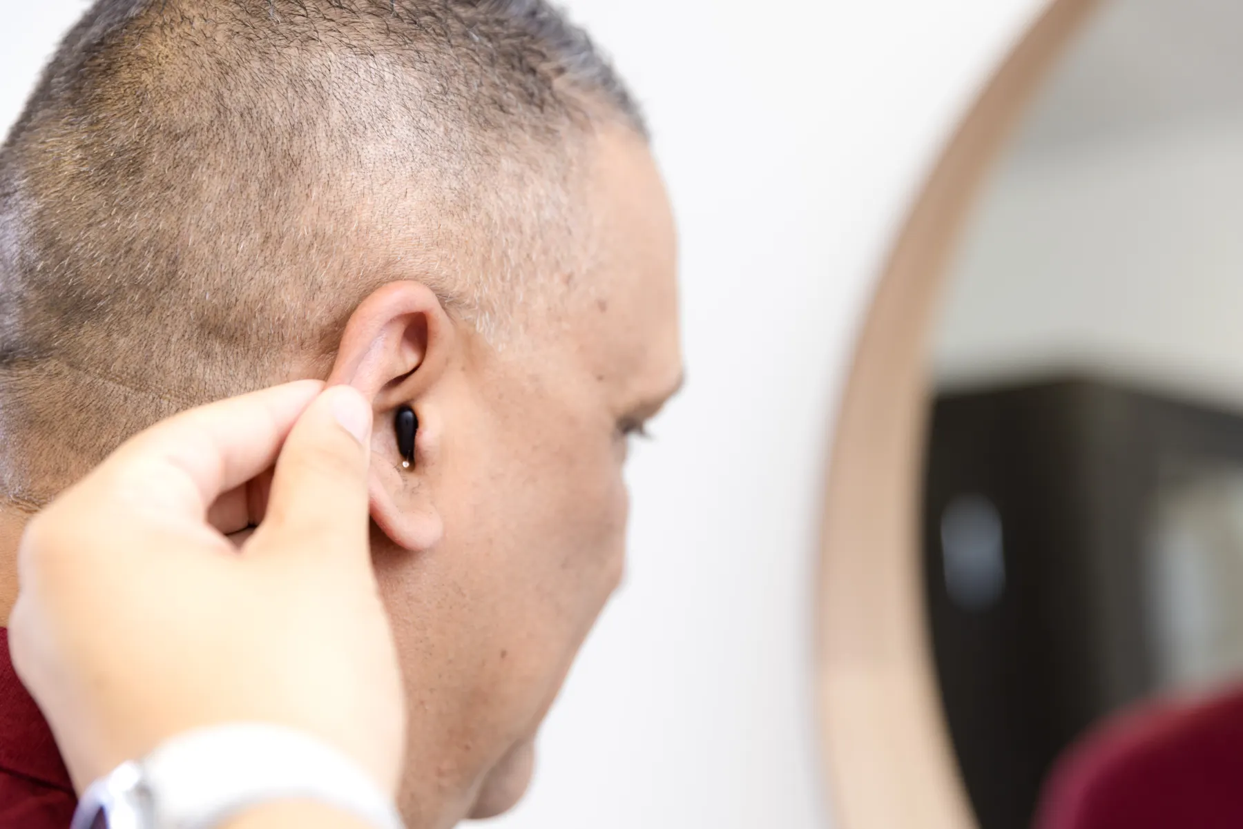 A new hearing aid being placed on a patient's ear, his reflection in the mirror