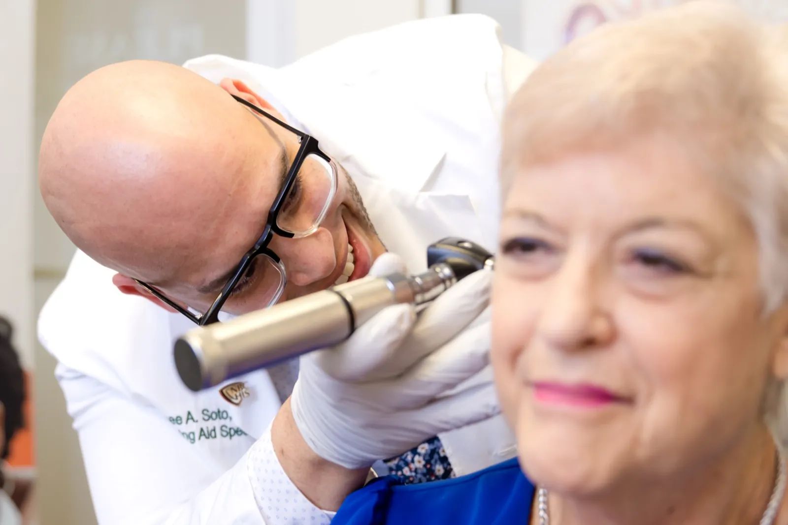 Jaysee Soto, Hearing Aid Specialist, checking a smiling patient's ear with a video otoscope